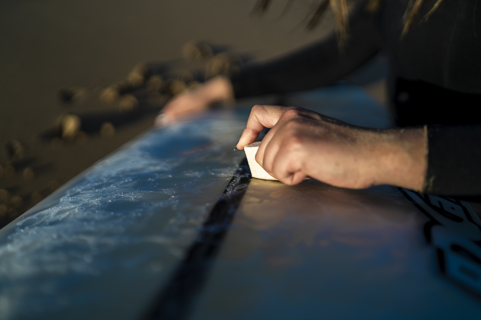 closeup-shot-female-waxing-her-surfboard-beach-spain_181624-23128